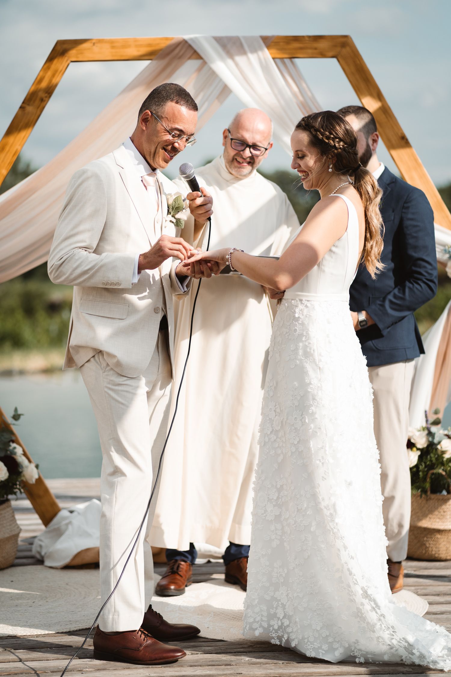 Bride and groom exchanging rings and laughing during outdoor wedding ceremony at hexagonal arch.