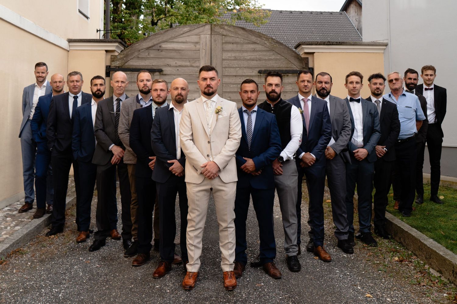 Groom stands confidently with groomsmen in suits posed together outdoors at a wedding venue.