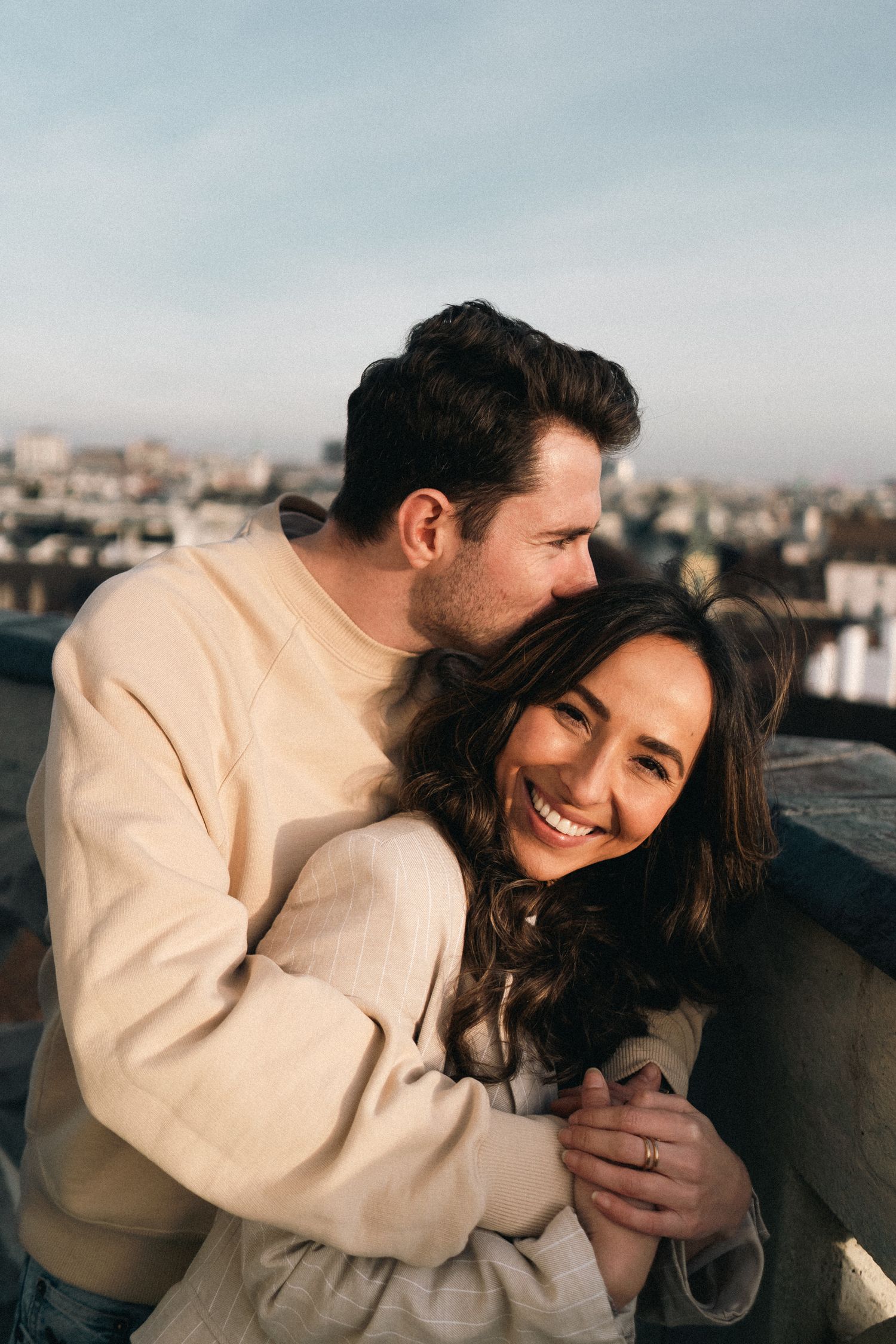 Happy couple embracing on Vienna rooftop at sunset with city skyline in background.