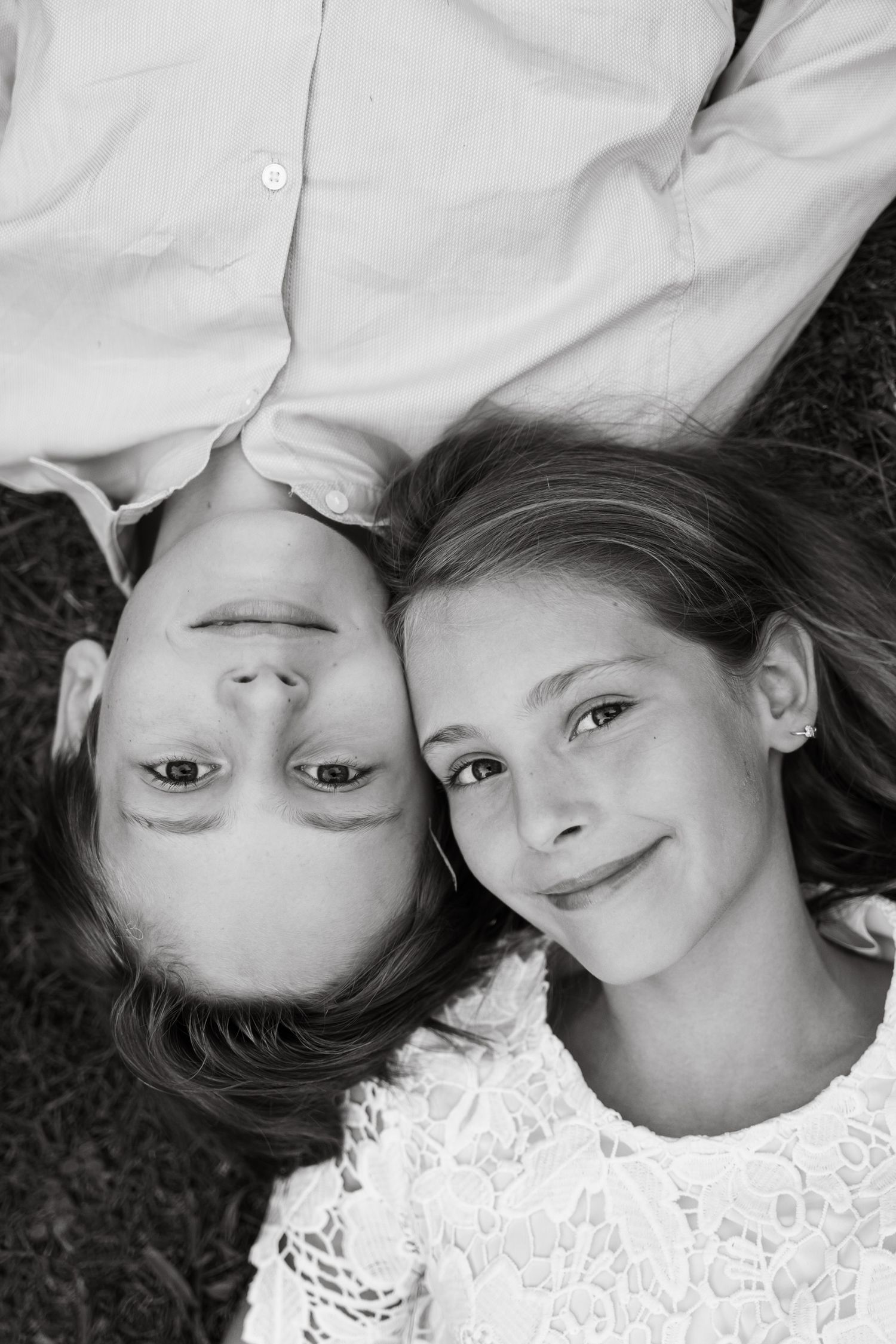 Black and white photo of two children lying on grass, smiling up at camera.