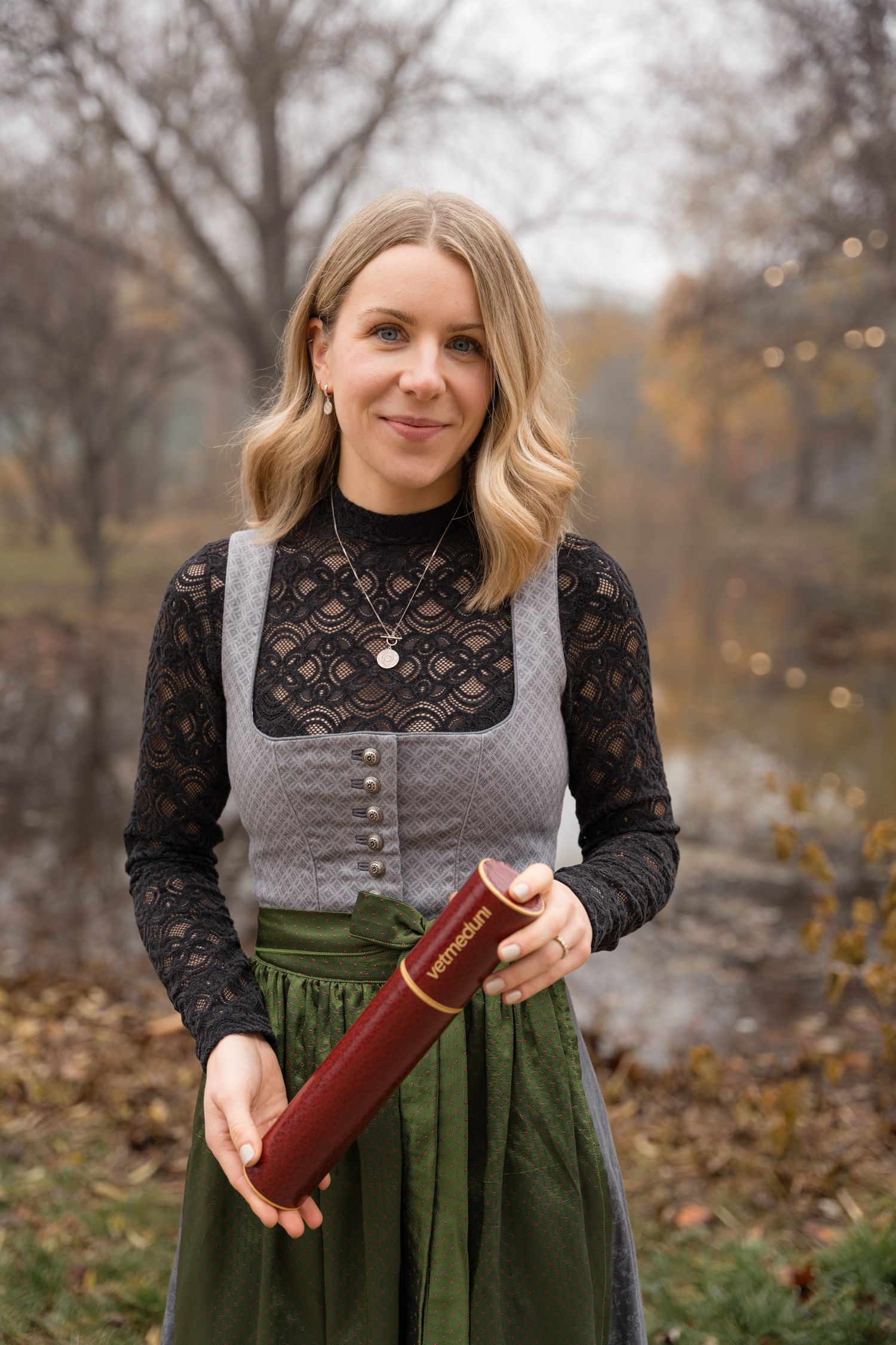 Blonde woman in traditional dirndl dress holding diploma tube at graduation ceremony.