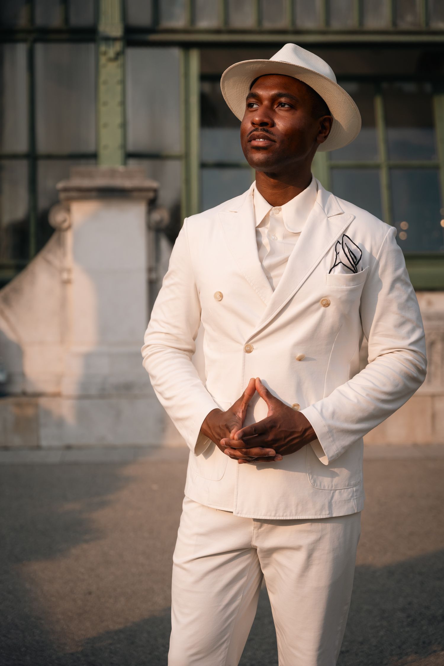 Stylish man in white double-breasted suit and panama hat posing outdoors.