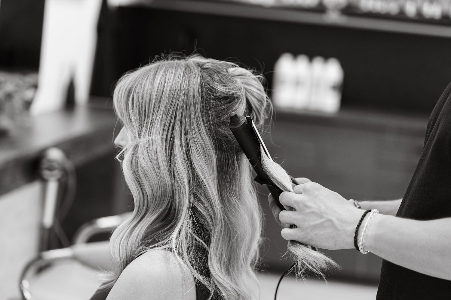 Black and white photo of hairstylist using flat iron on blonde hair.
