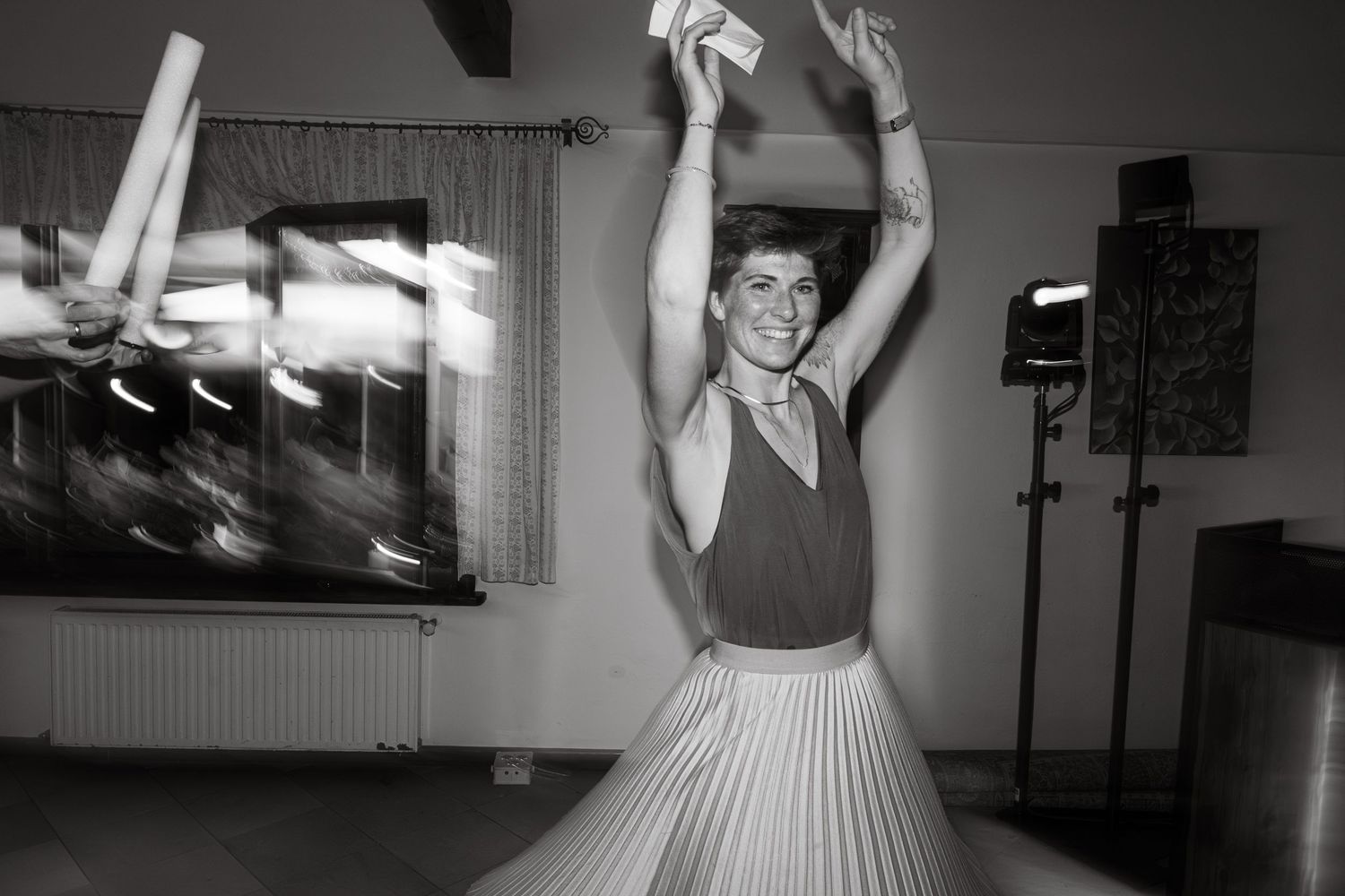 Black and white photo of a woman dancing energetically with arms raised at a wedding celebration.