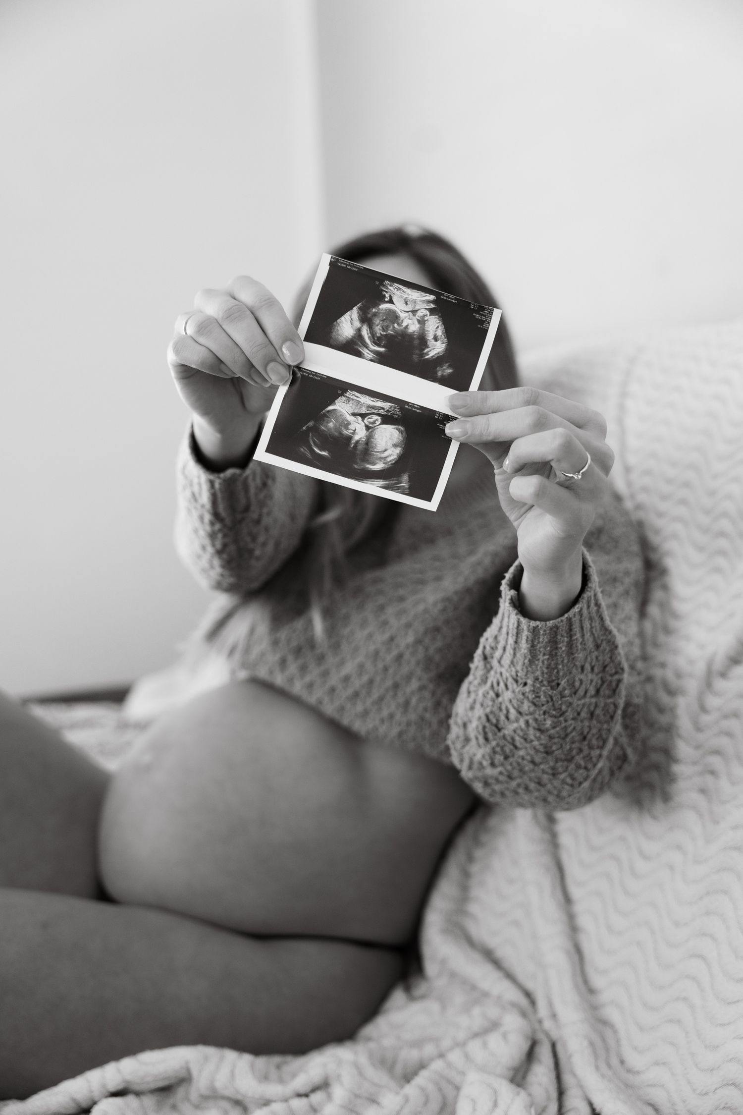 Black and white photo of pregnant woman holding ultrasound scans in front of face.