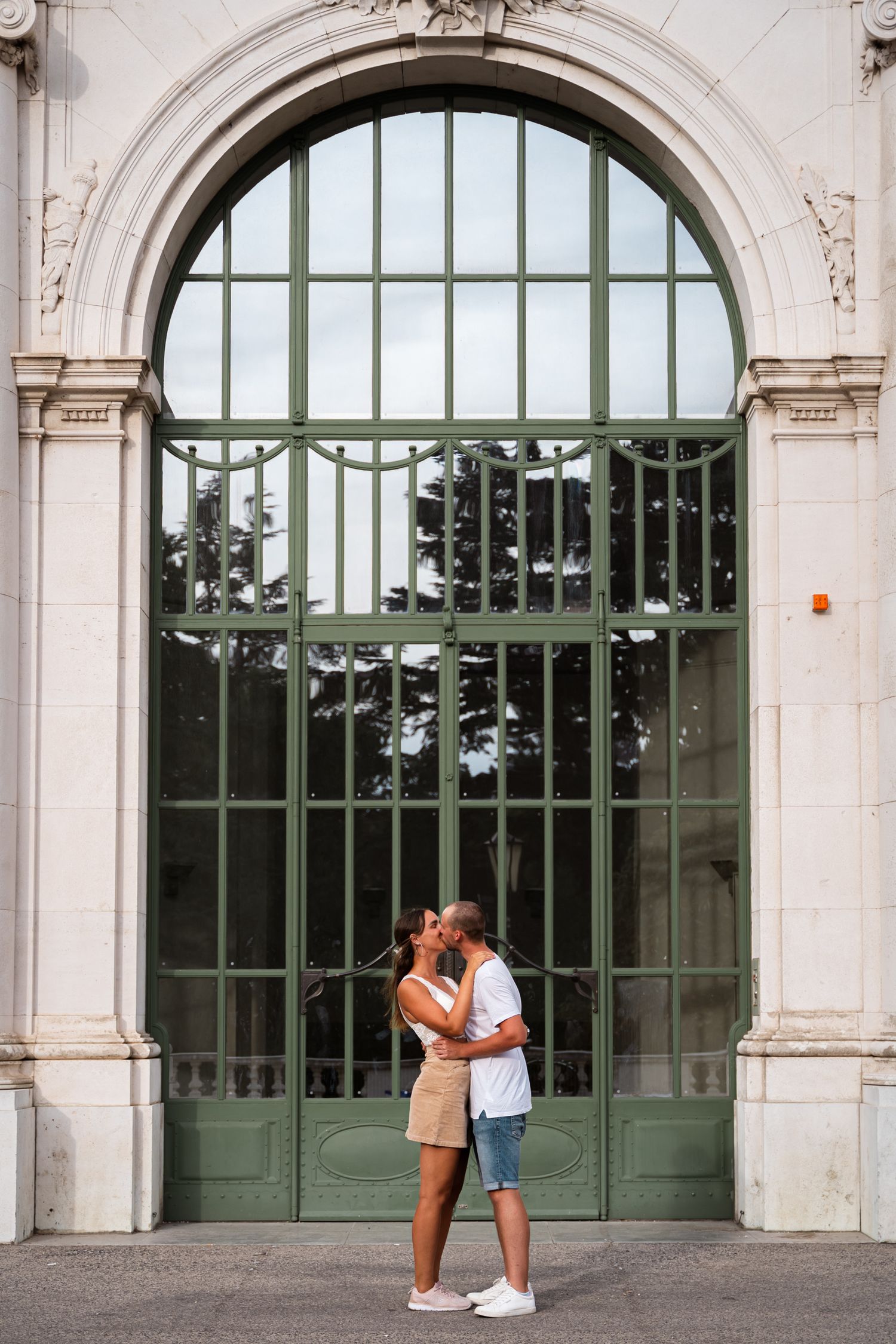 Couple sharing a kiss in front of a large ornate green arched door on a building.