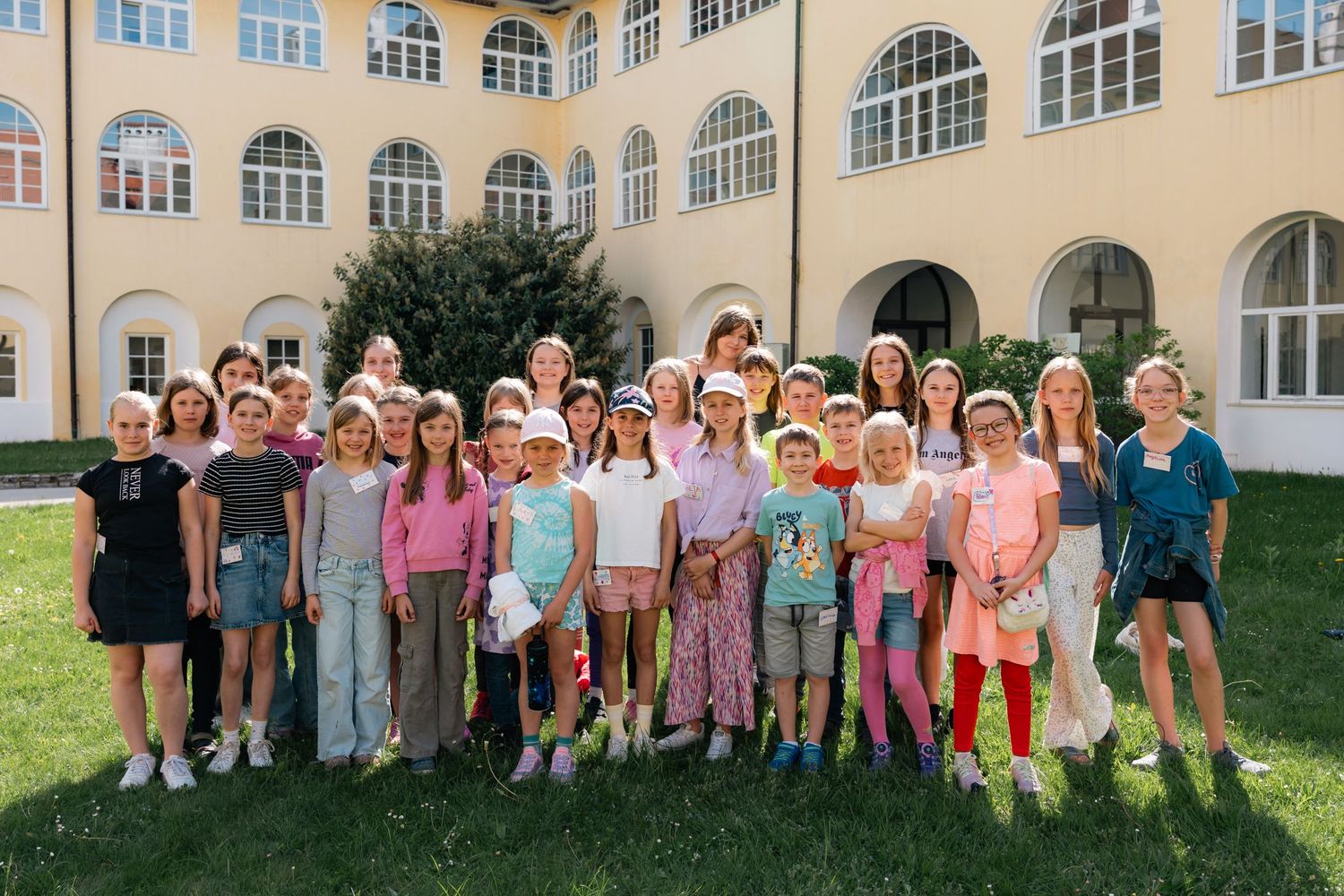 Large group of smiling children and adults posing in courtyard of a yellow historic building.