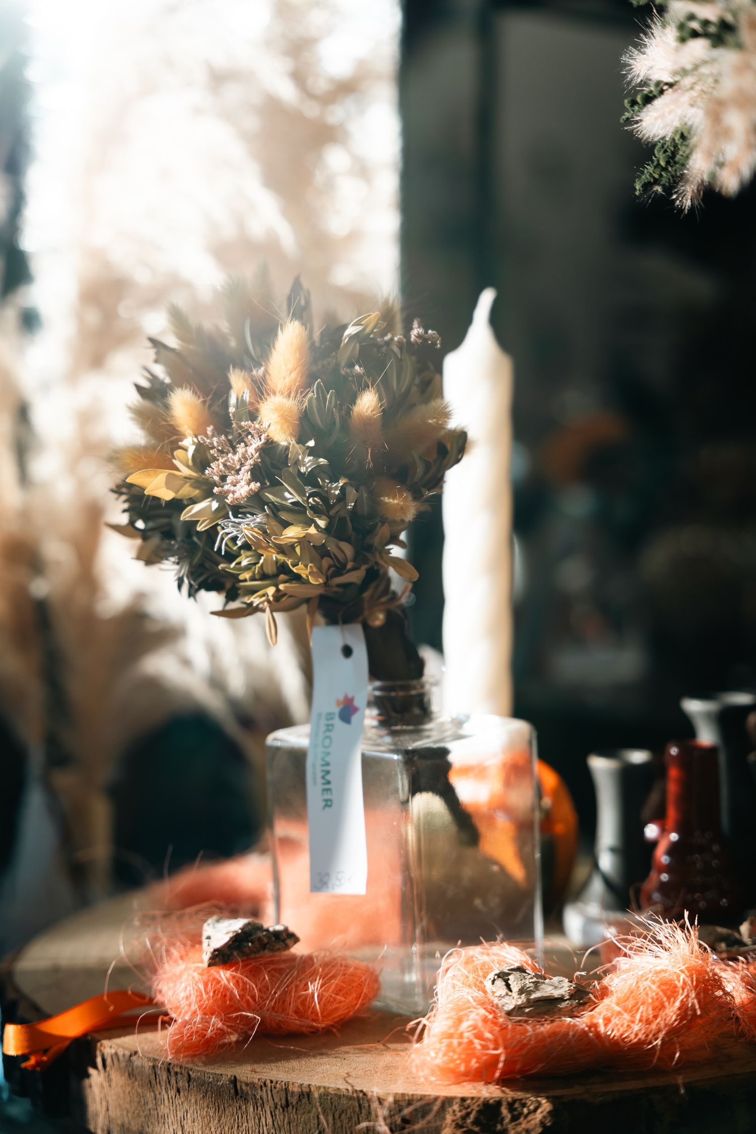 Dried floral arrangement in a glass jar with orange decorative accents on a wooden surface.