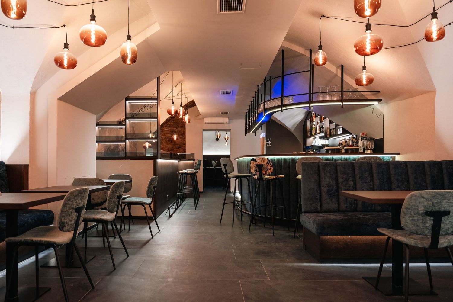 Modern bar and restaurant interior with warm Edison bulb lighting, dark furniture, and vaulted white ceilings.