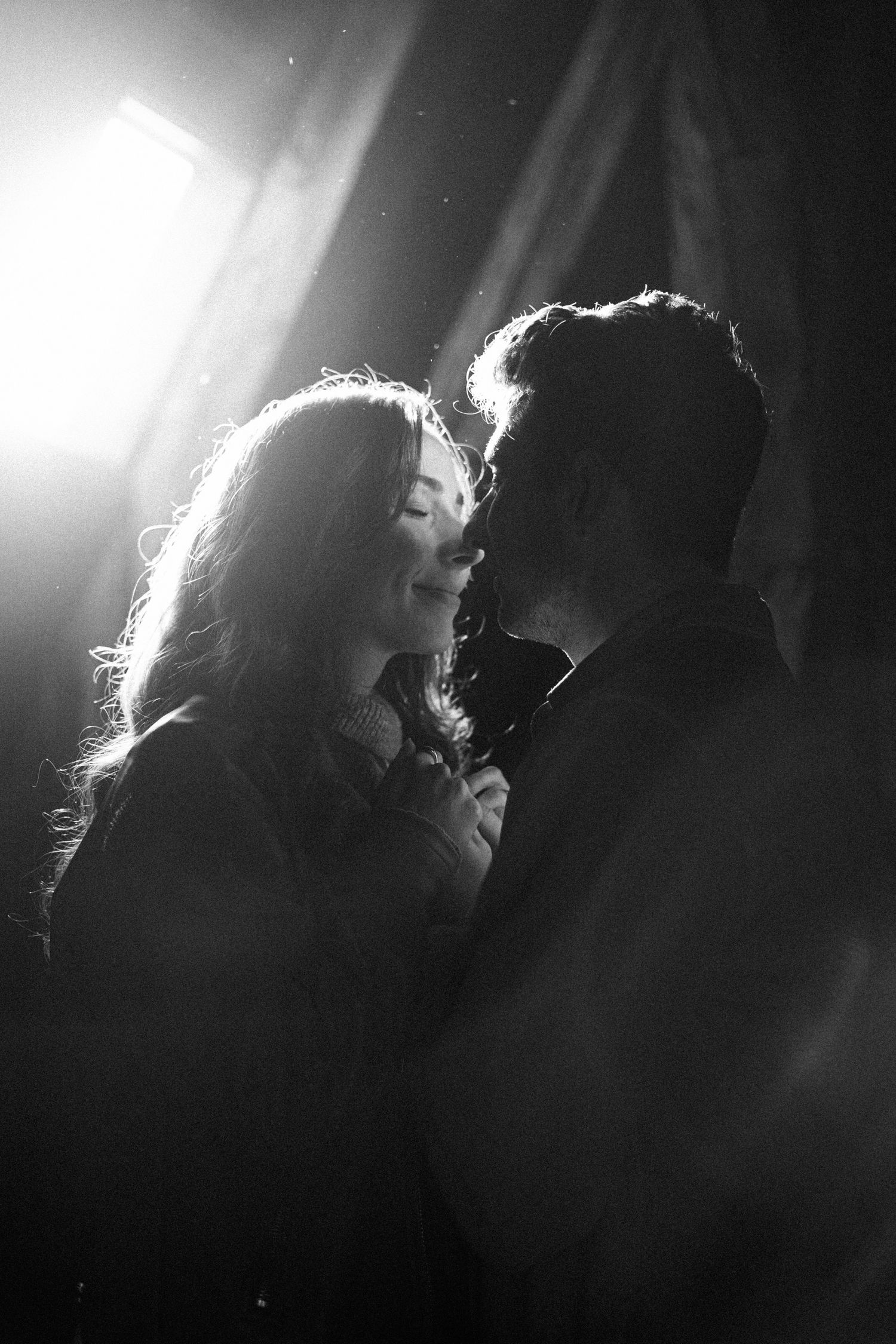 Romantic black and white silhouette of couple kissing in dramatic backlight with lens flare.