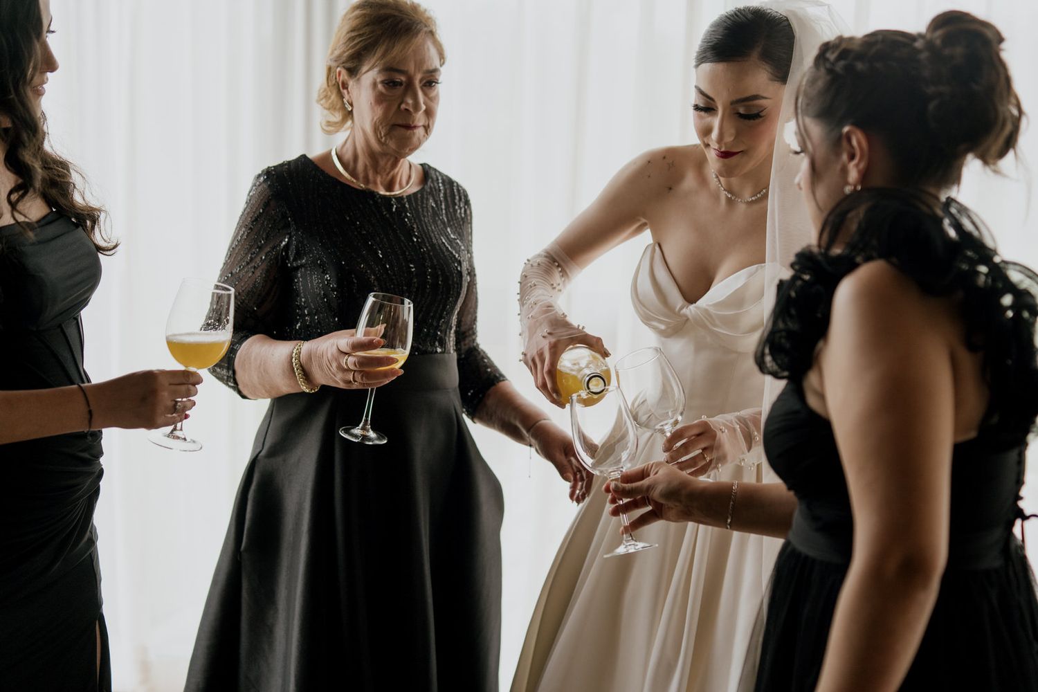 Group of people in formal attire sharing drinks and conversation by window.