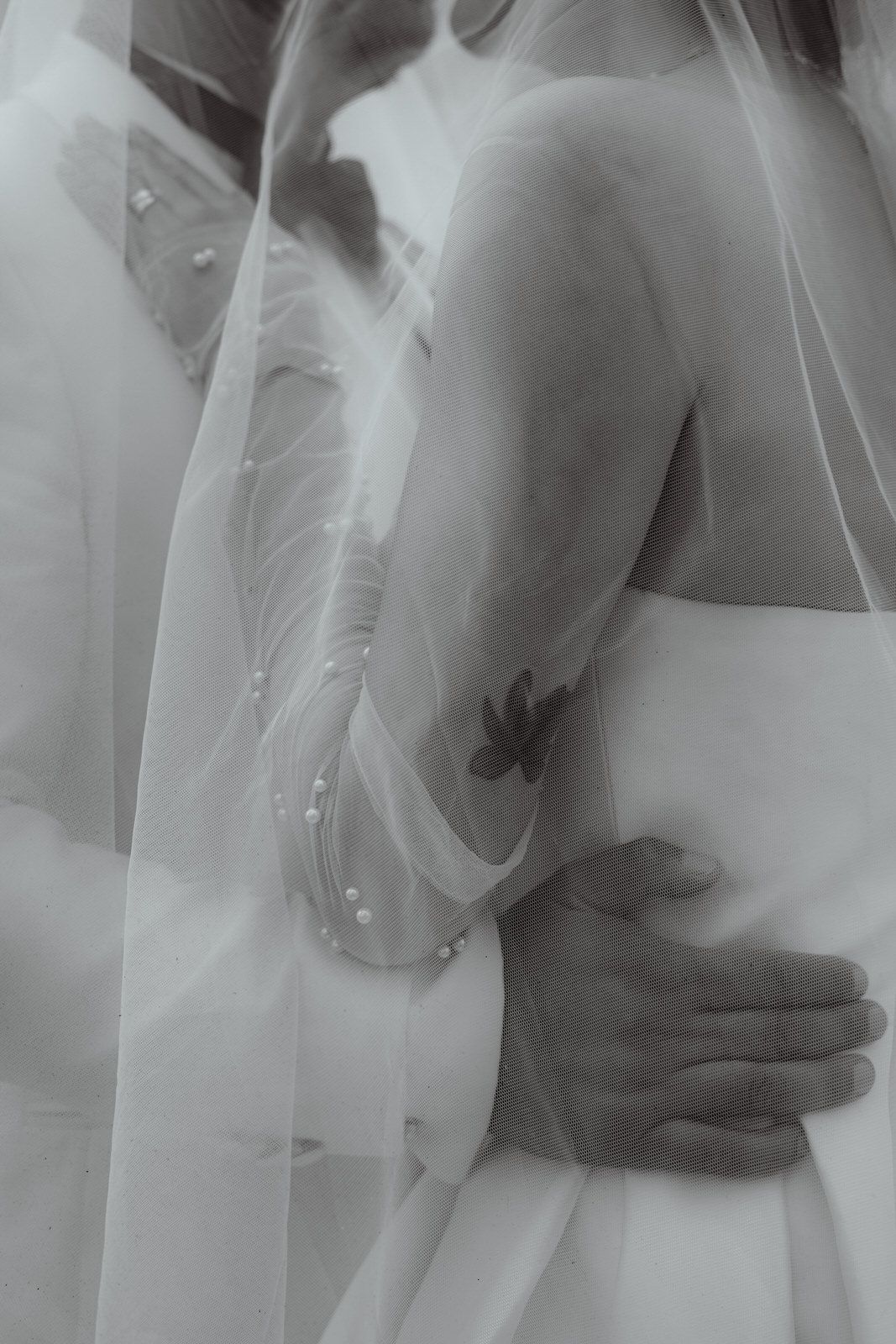 Black and white artistic photo showing intimate embrace with flowing wedding veil.