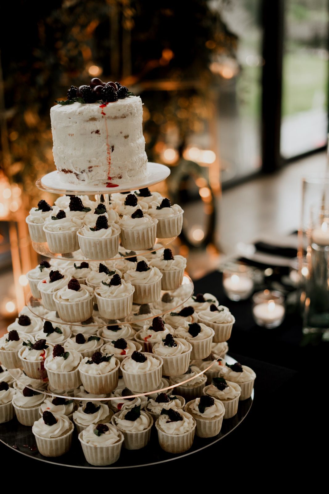 Multi-tiered white cupcake display with dark berry toppings illuminated by warm lighting.