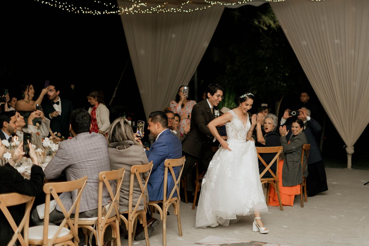 Wedding reception celebration under a canopy of string lights and white draping.