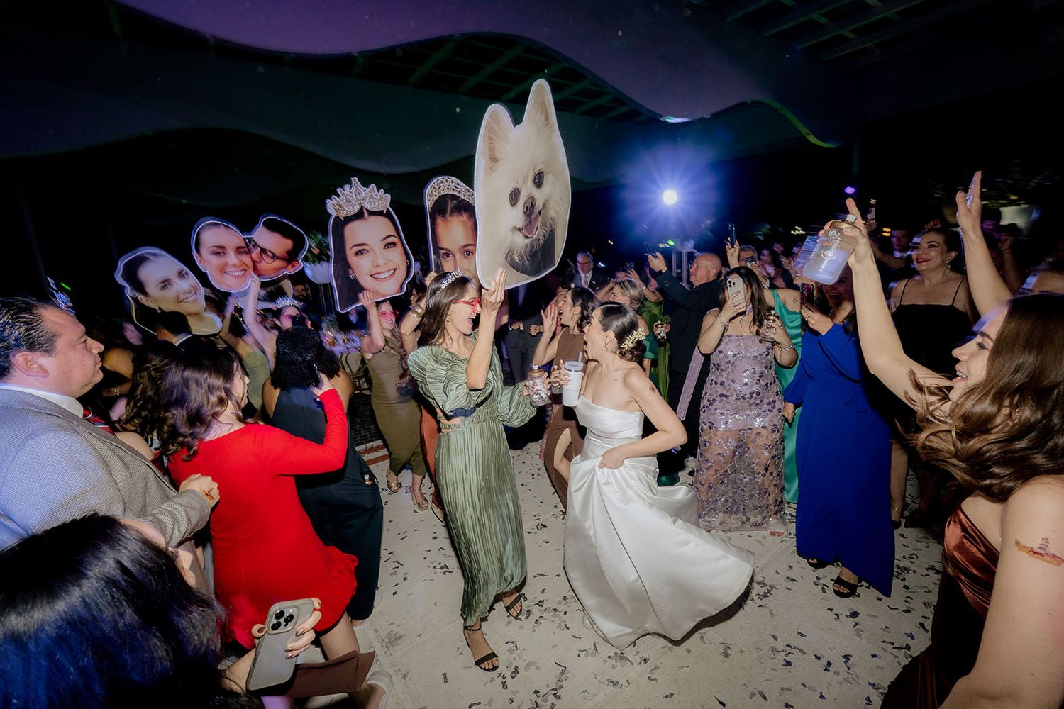 Bride dancing with guests holding photo booth props at a lively wedding reception party.