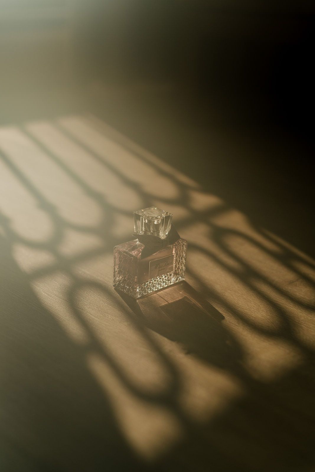 Crystal perfume bottle casting elegant shadows in warm golden light on a textured surface.