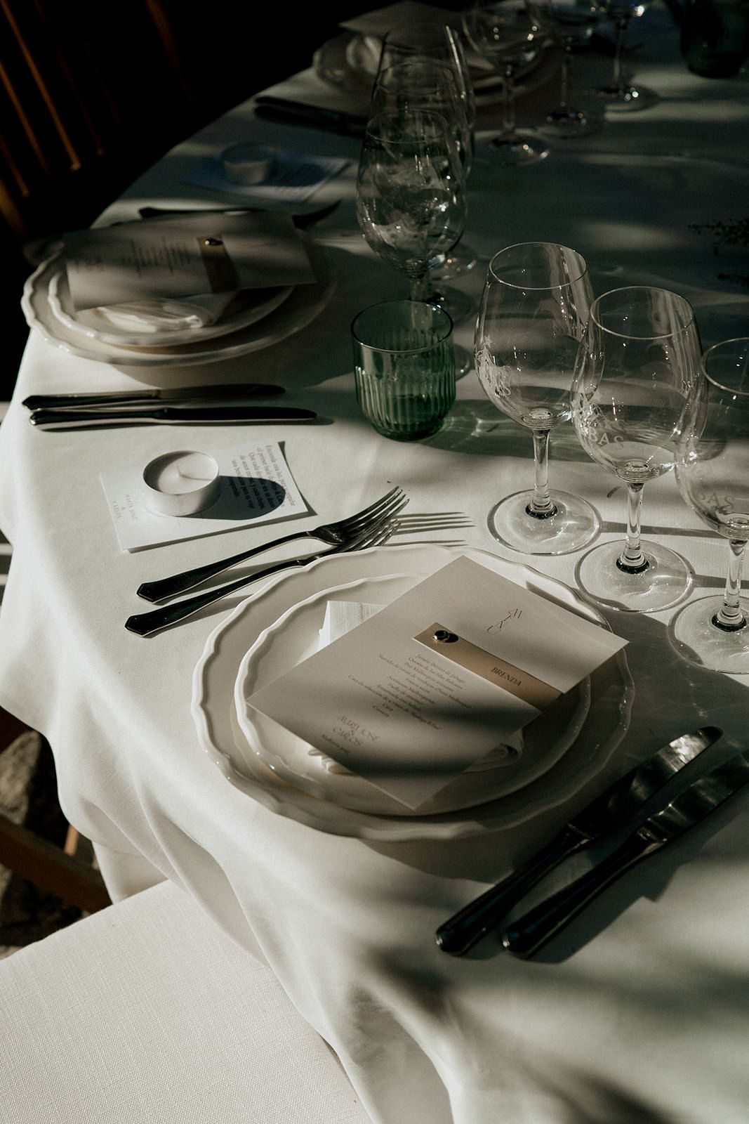 Formal place settings with wine glasses and cutlery on crisp white tablecloth.