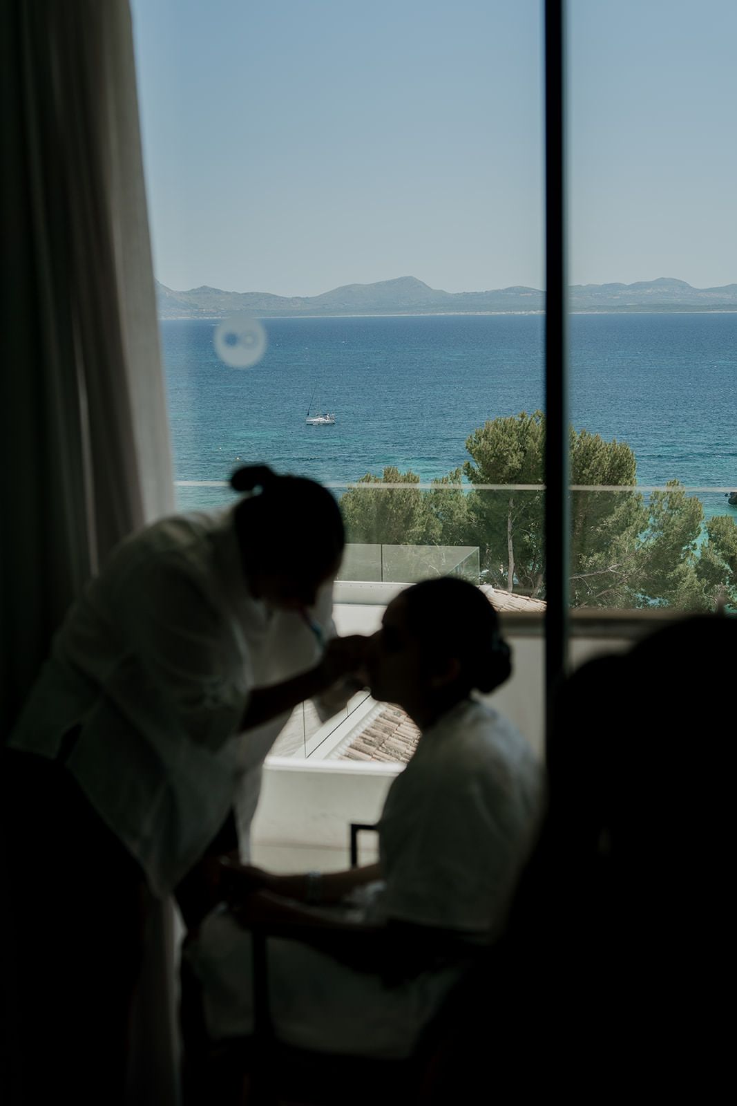 A series of silhouettes against a window overlooking a serene ocean view with mountains in the distance.