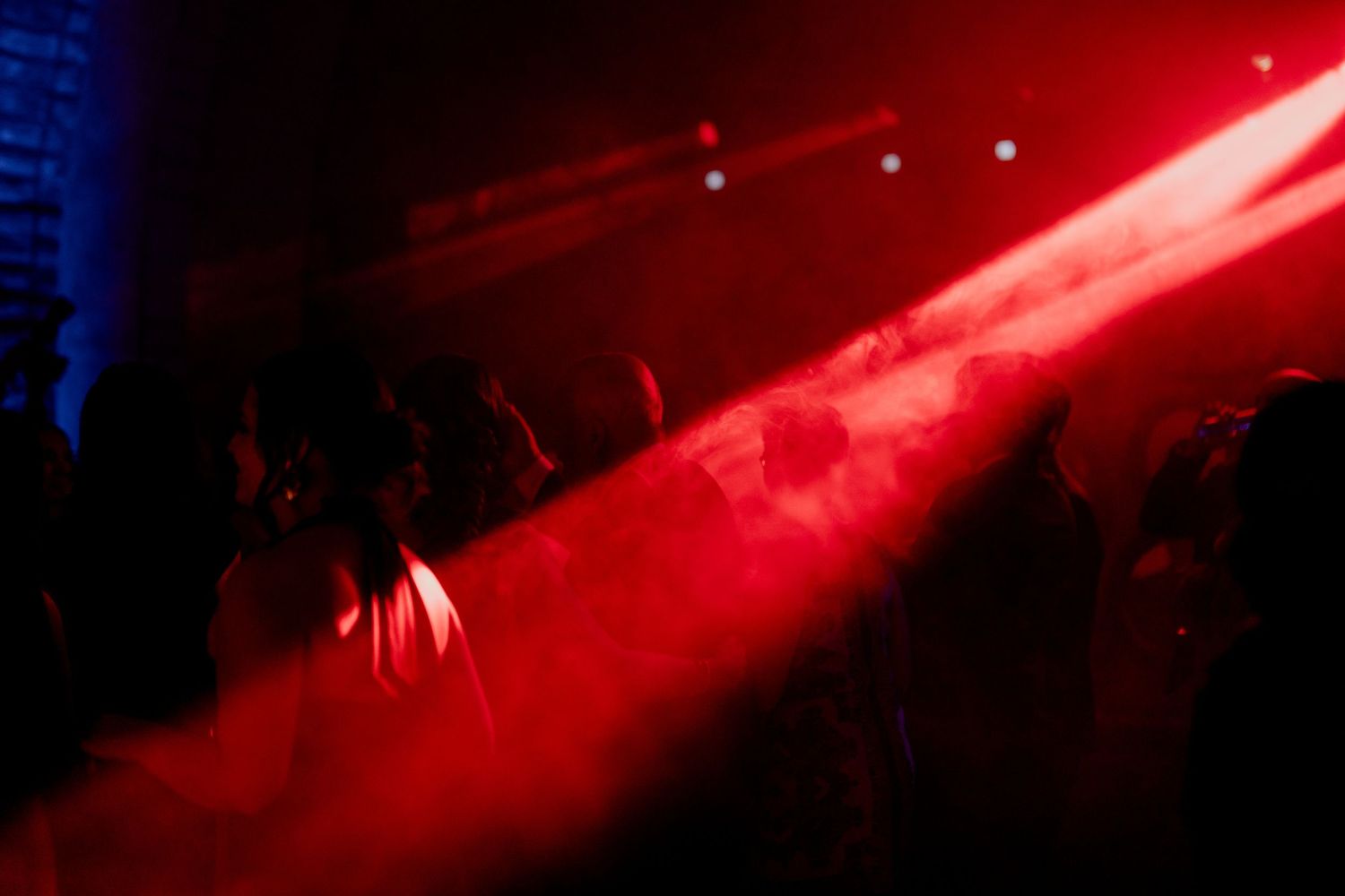 Red stage lighting illuminates a dark dance floor filled with party guests.