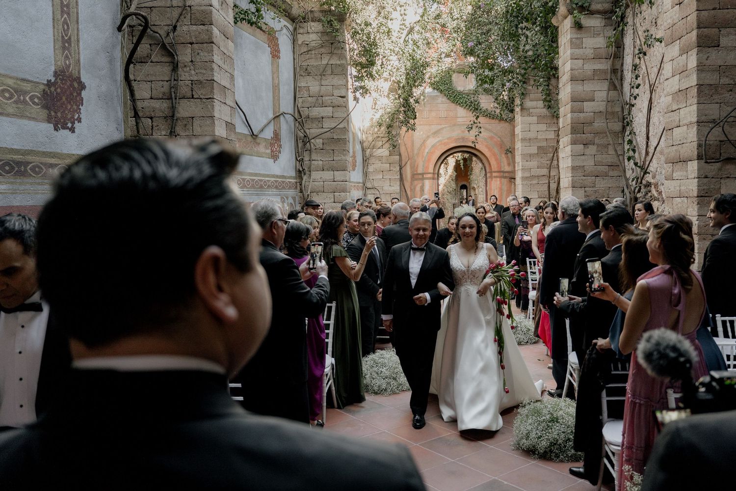 Wedding ceremony in progress at stone church with gathered guests.