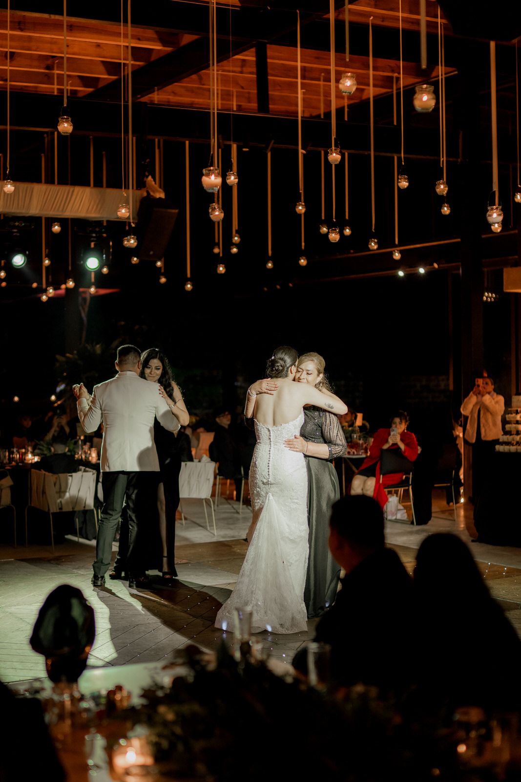 Wedding couples dancing together under romantic string lights at evening reception.