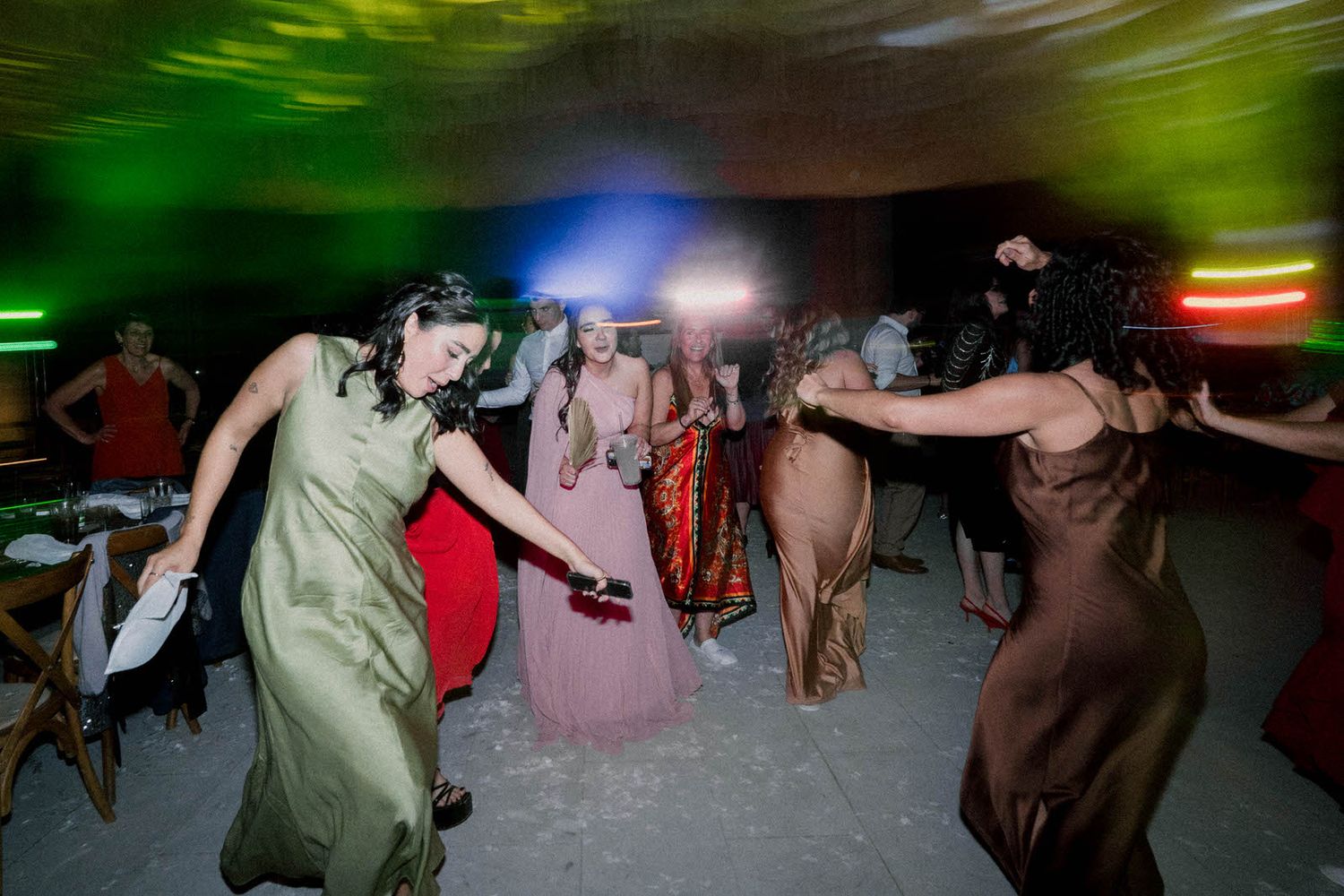 Party guests dance energetically in formal dresses under colorful lighting.