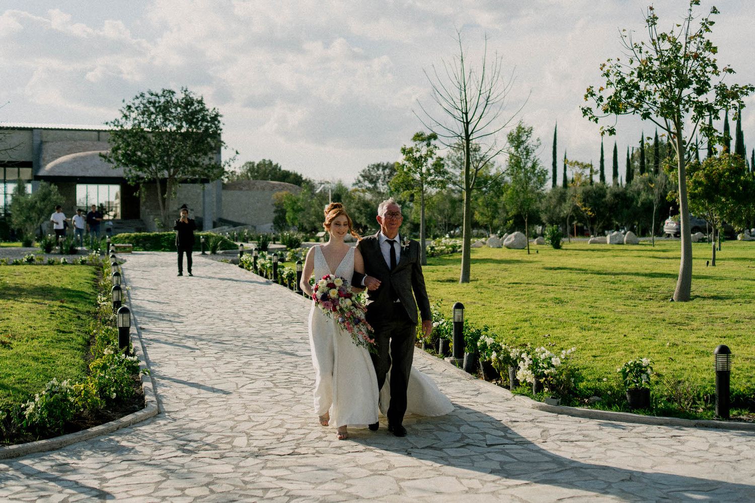 Stone pathway leads to covered outdoor wedding venue with guests gathered for ceremony.