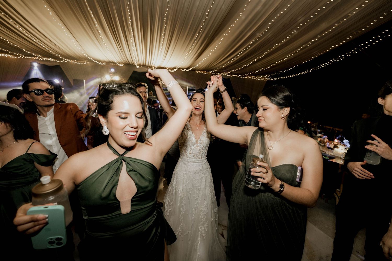 Wedding reception guests dance and celebrate under elegant draped fabric ceiling with twinkling lights.