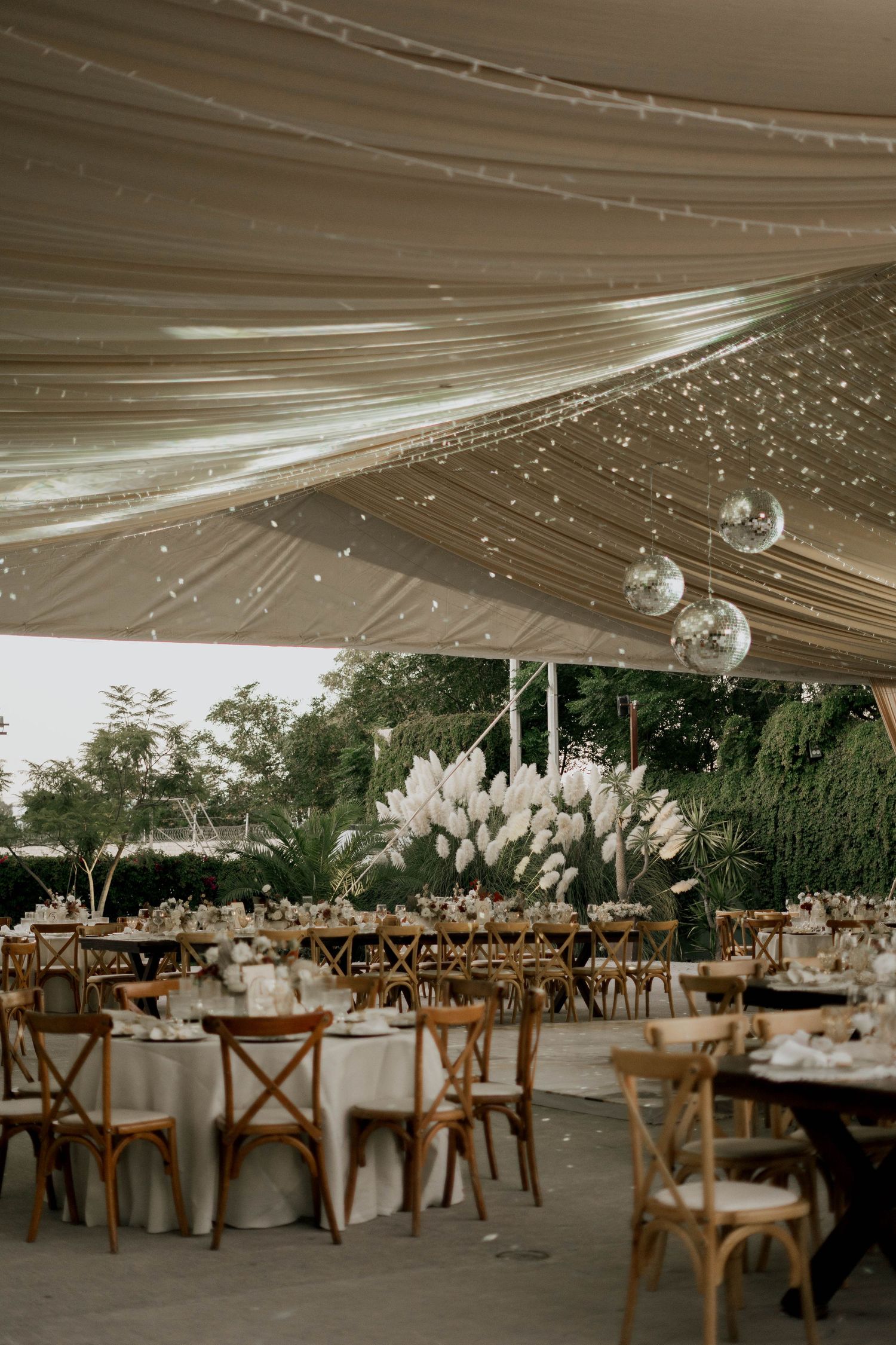 Elegant outdoor wedding reception setup with wooden chairs and white tent canopy.