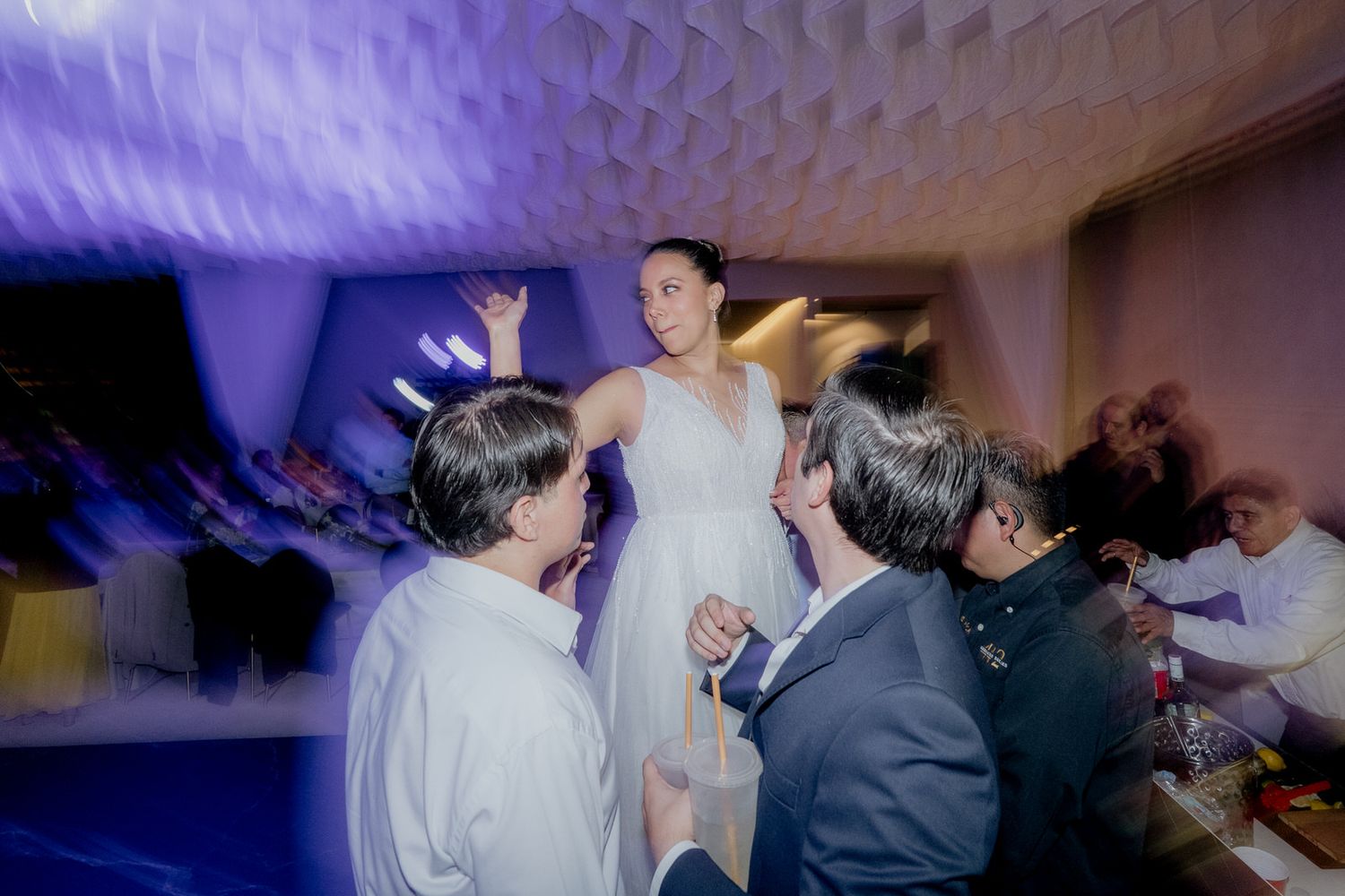 Bride in white dress stands elevated while guests socialize below at a wedding reception.