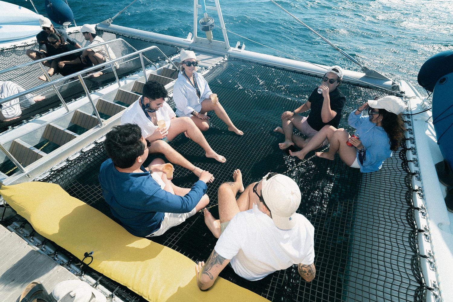 People relaxing on a catamaran's mesh netting over blue ocean waters during a sailing excursion.