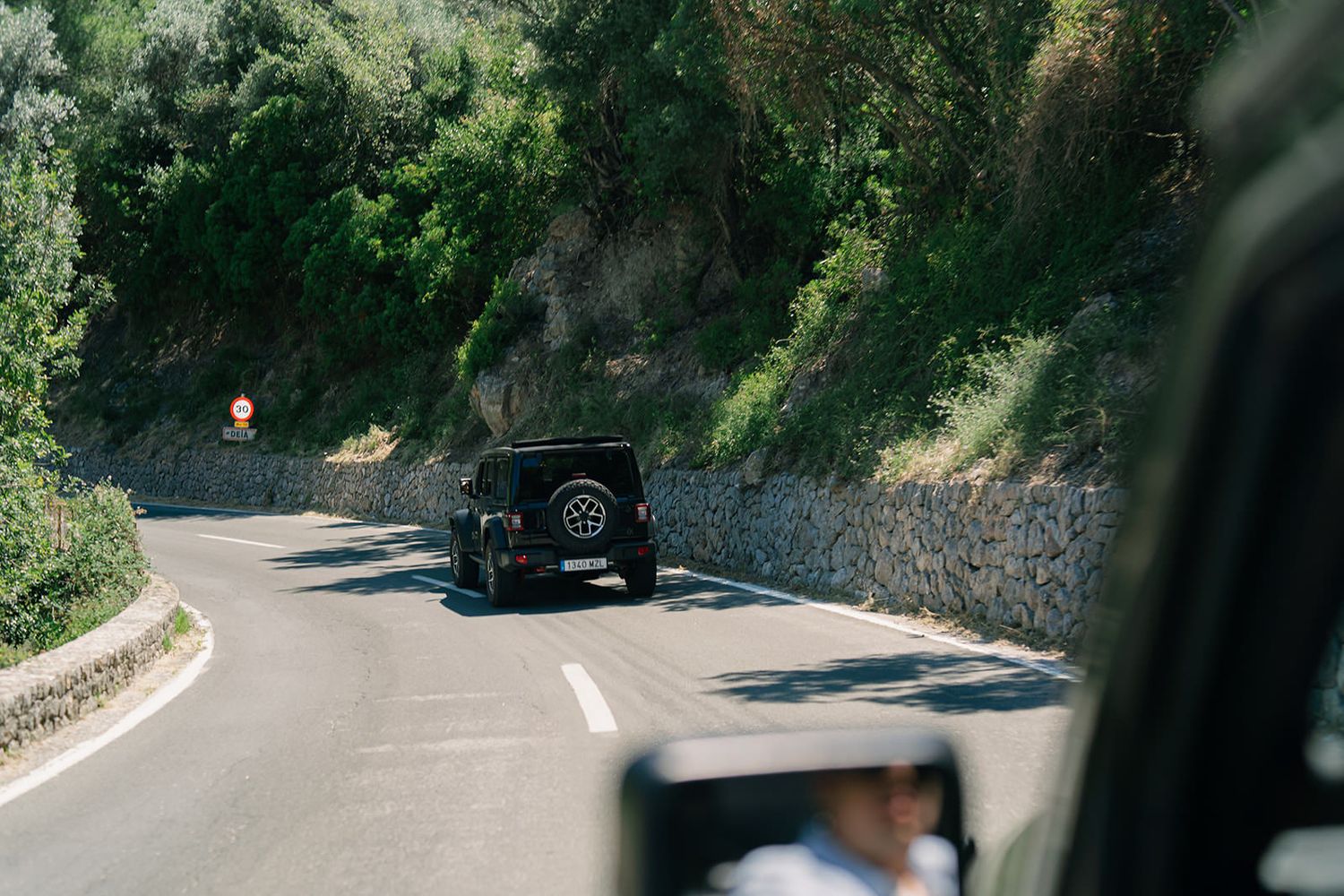 Winding mountain road through dense forest with a black vehicle visible in the distance.