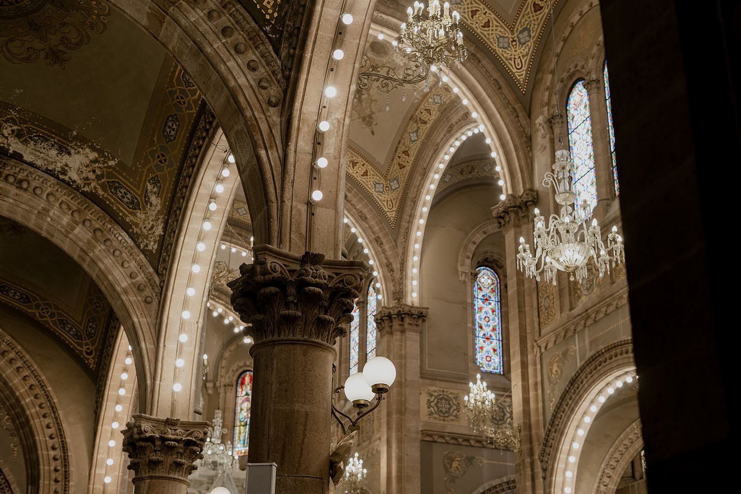 Ornate cathedral interior with grand arches, crystal chandeliers, stained glass windows, and intricate stone columns.
