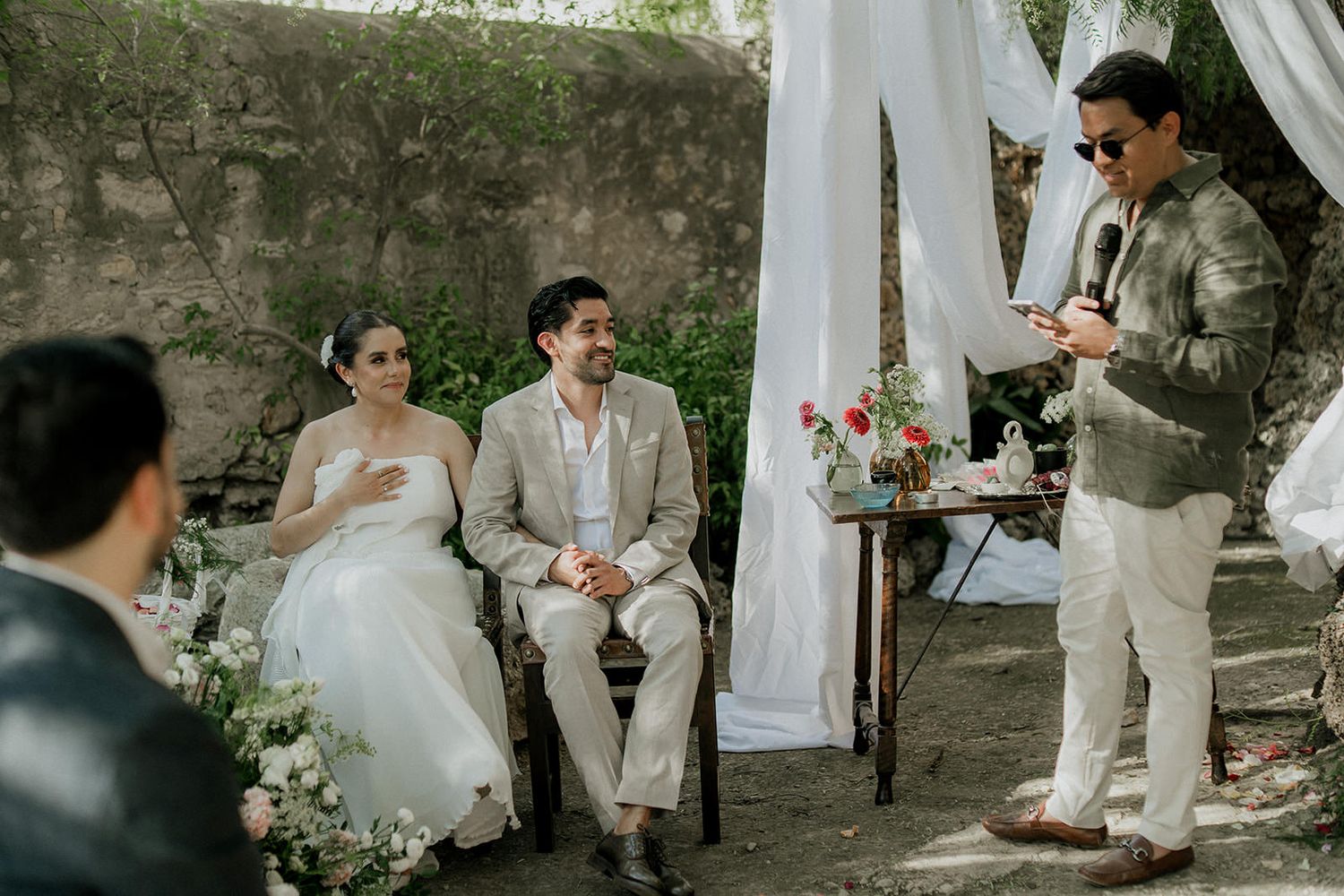 A romantic outdoor wedding ceremony with white fabric draping and floral arrangements in a natural setting.