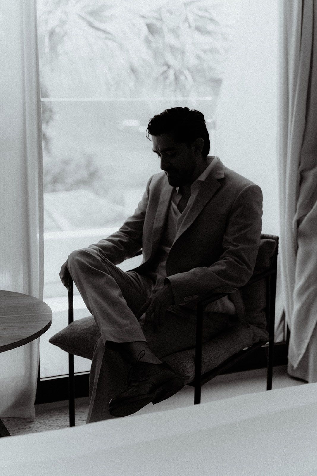 A silhouette of a person in a light suit sitting thoughtfully by a window in black and white.