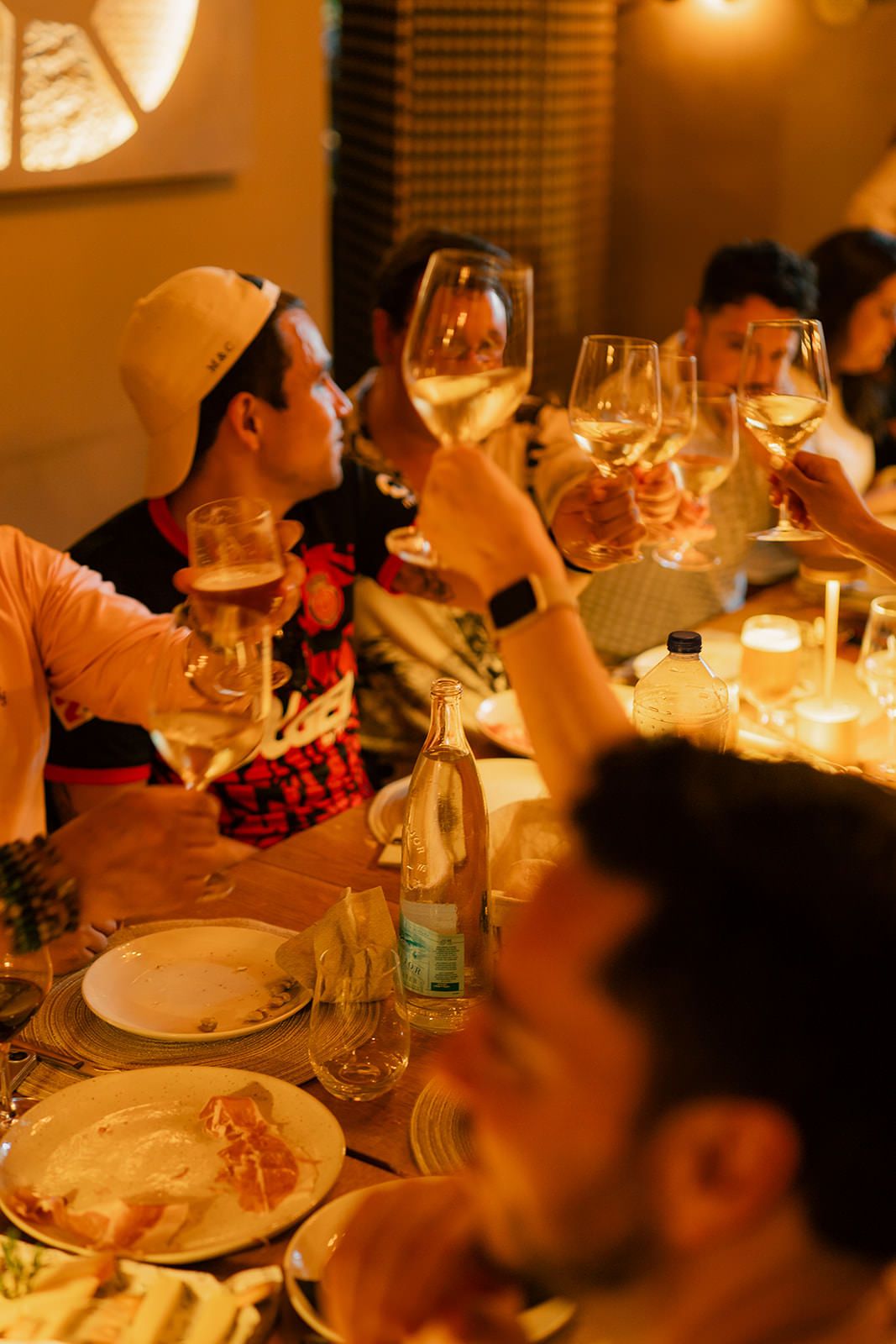 Diners enjoy an intimate candlelit dinner gathering with wine glasses and plates visible in warm ambient lighting.