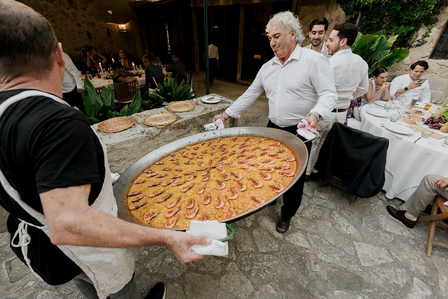 People gathered around a large paella pan being served at an outdoor event.