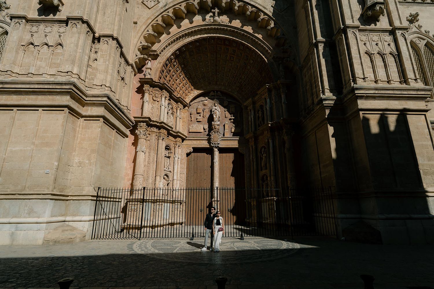 Gothic stone archways and columns create dramatic shadows in a historic European cathedral corridor.