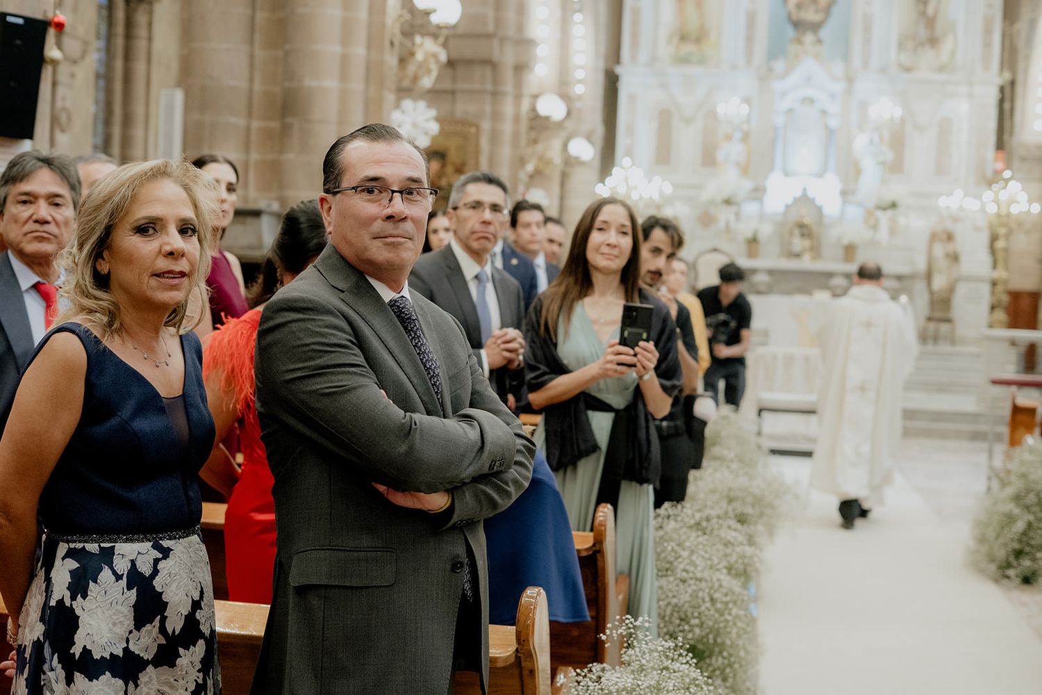 Guests standing and watching a wedding ceremony inside an elegant church with ornate architecture.