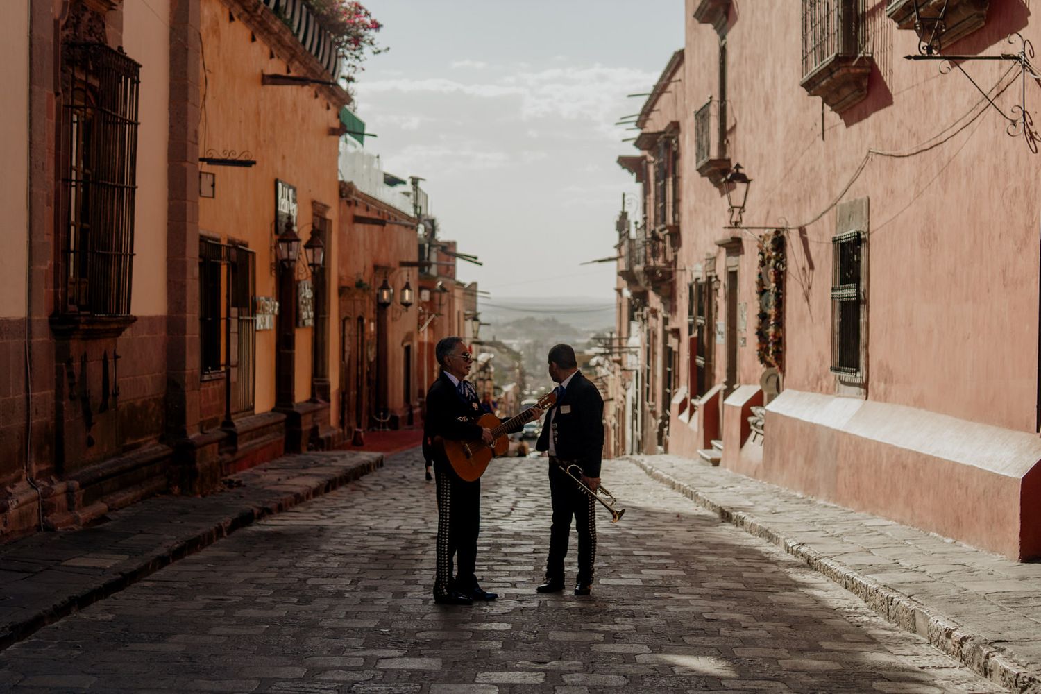 Two people standing on a cobblestone street in a colorful Mexican town.