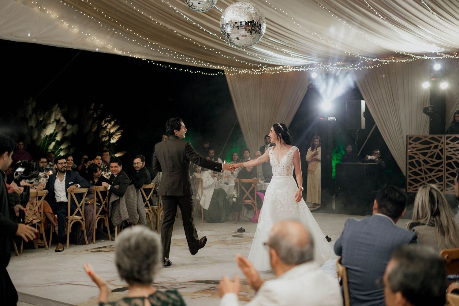 Wedding reception guests dancing on a white dance floor under a draped tent ceiling with disco ball.