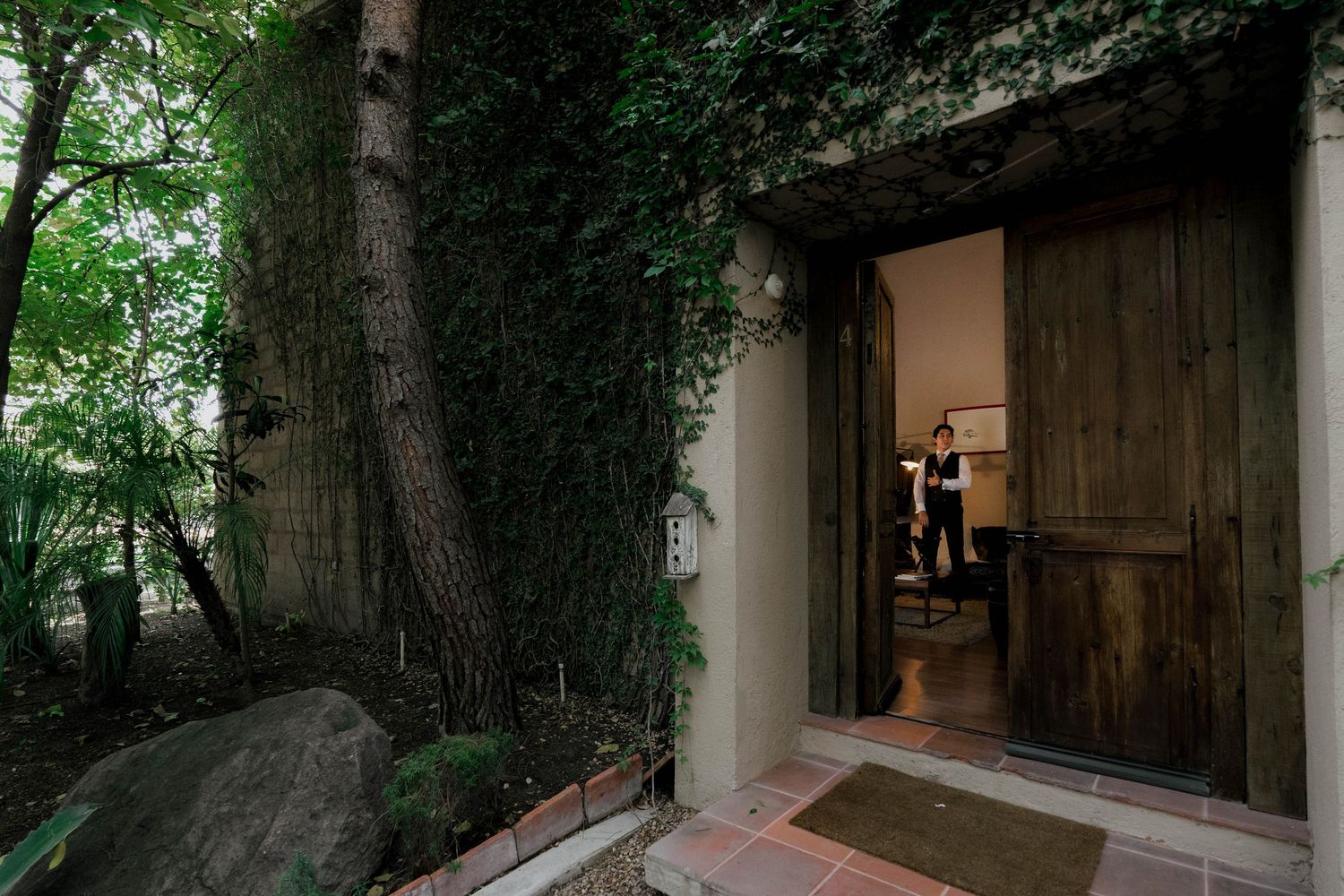 Lush green garden pathway with stone columns and overhanging trees creating a natural archway.