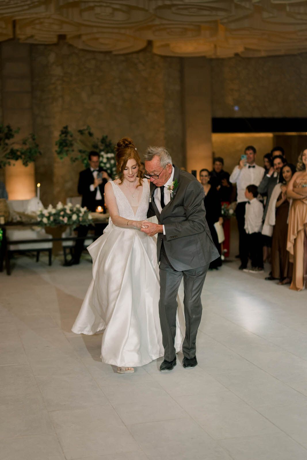 Couple performs their first dance on an elegant white dance floor surrounded by guests.