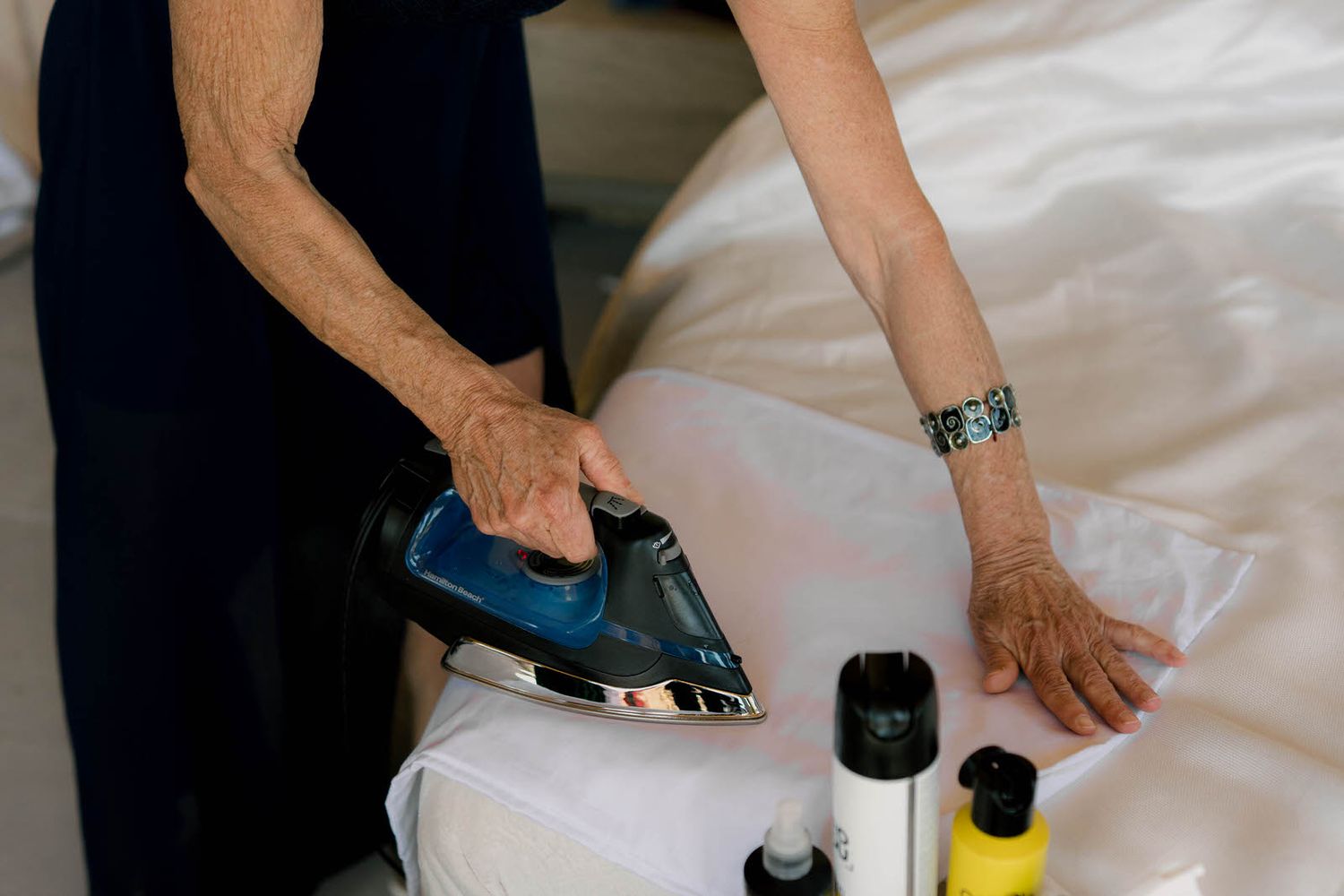 Close-up shots of hands steaming and pressing white fabric on a table.