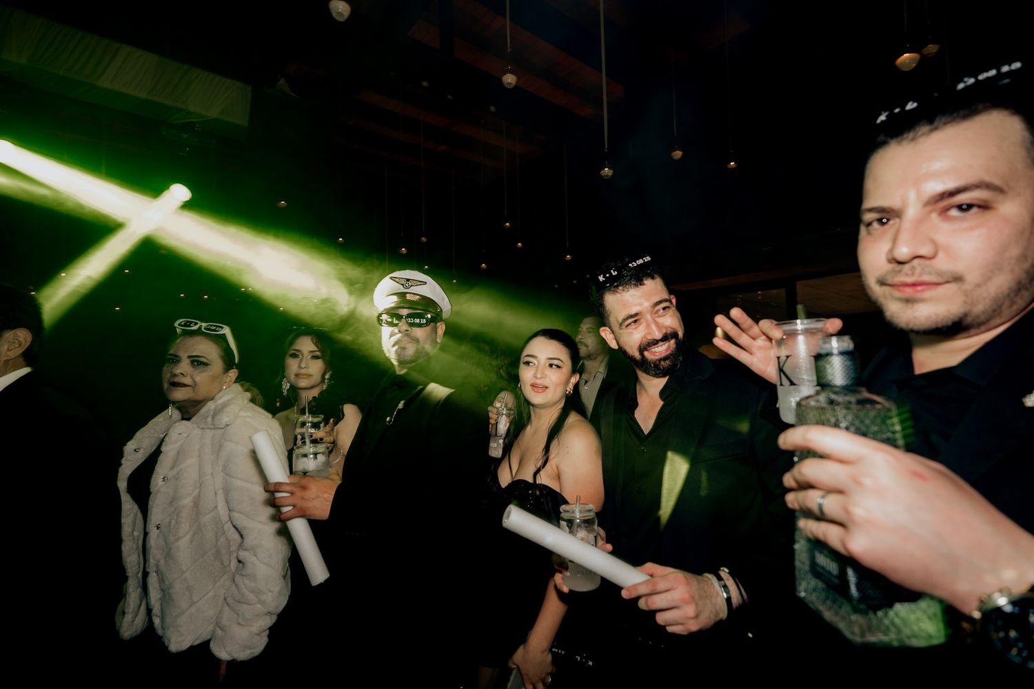 Green laser lights illuminate dancers at a lively indoor party venue.