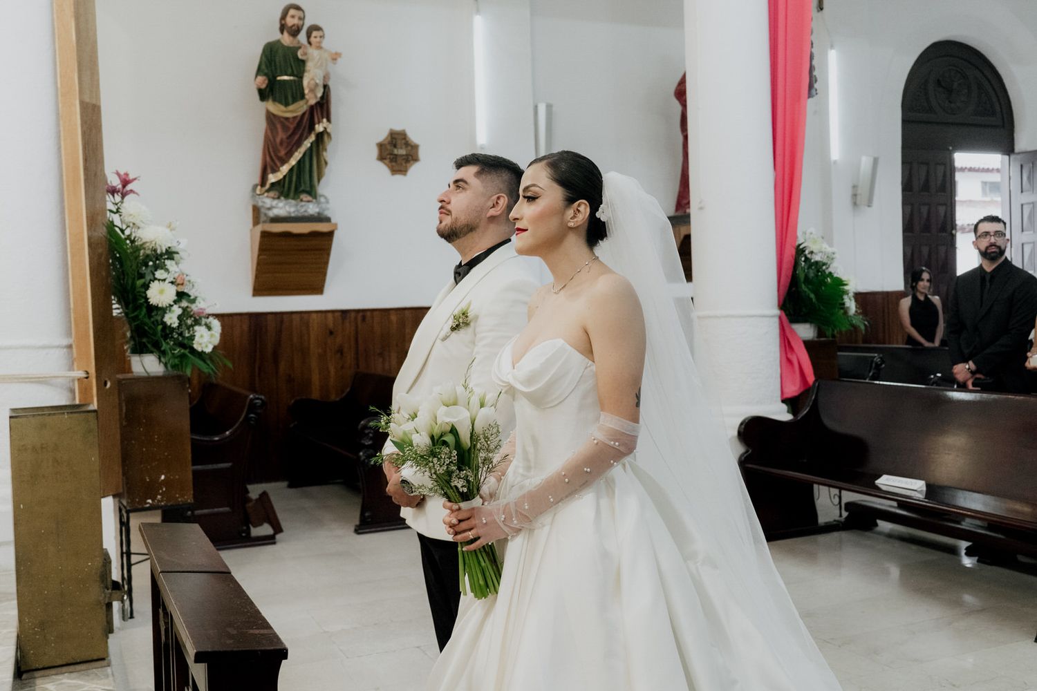 A couple stands at the altar during their wedding ceremony in a traditional church setting.