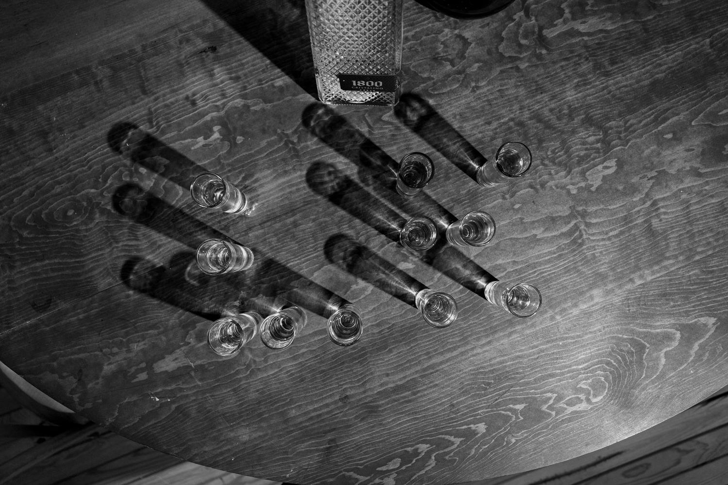 Black and white image of wine glasses and bottles arranged on a wooden surface.