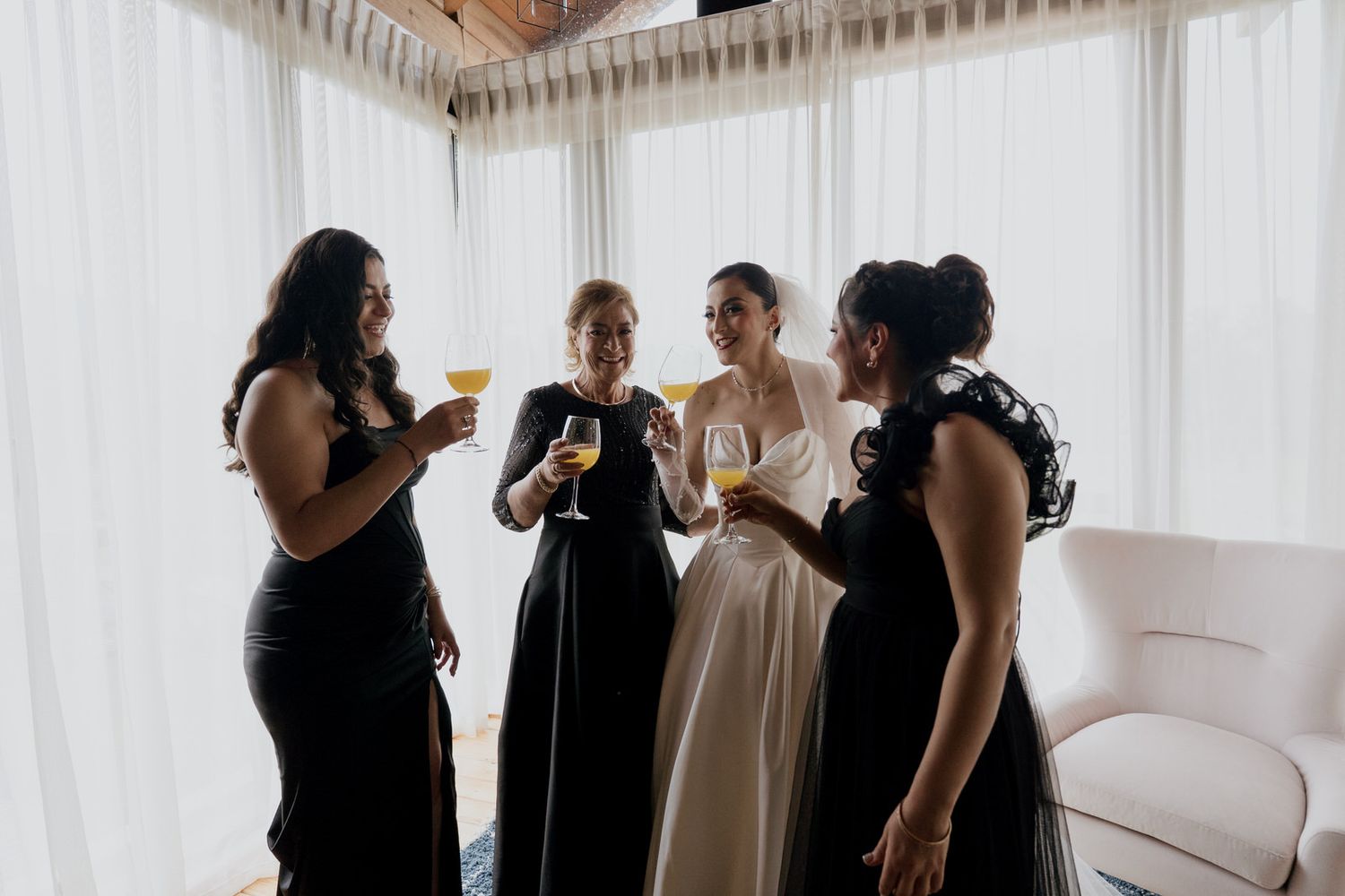 Group in formal attire enjoying drinks and conversation in bright corner room.