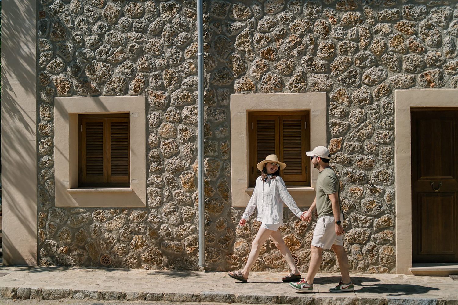 Sequence of stone building exterior shots showing people walking past rustic walls with wooden doors and windows.