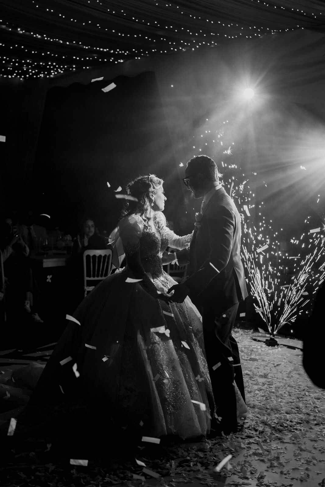 Dramatic black and white photo of couple's first dance under twinkling lights and spotlights.